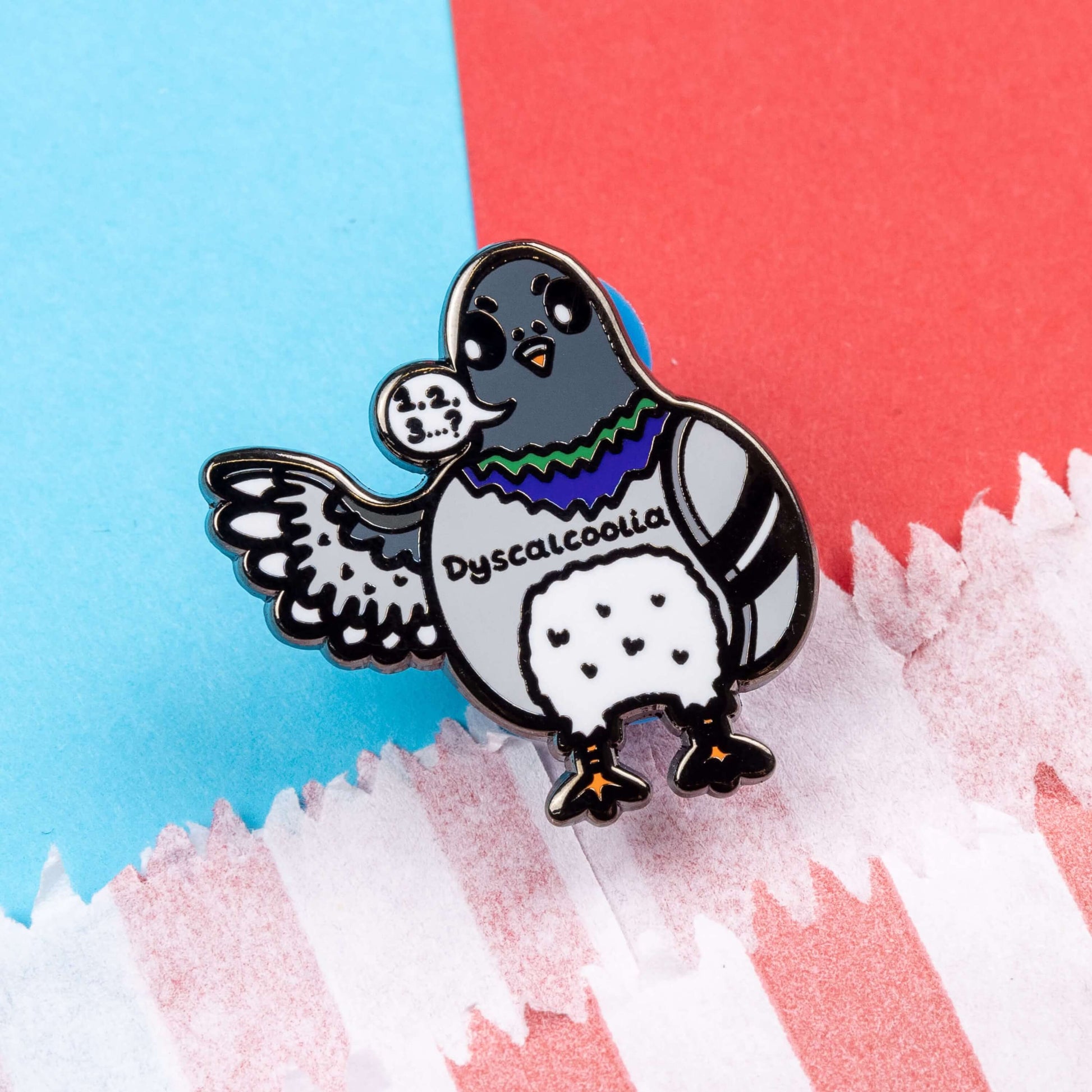 The Dyscalcoolia Pigeon Enamel Pin - Dyscalculia on a red and blue background. A Pigeon looking confused holding up a wing with a speech bubble full of numbers and a question mark across its chest reads 'dyscalcoolia'. The enamel pin is raising awareness for dyscalculia.