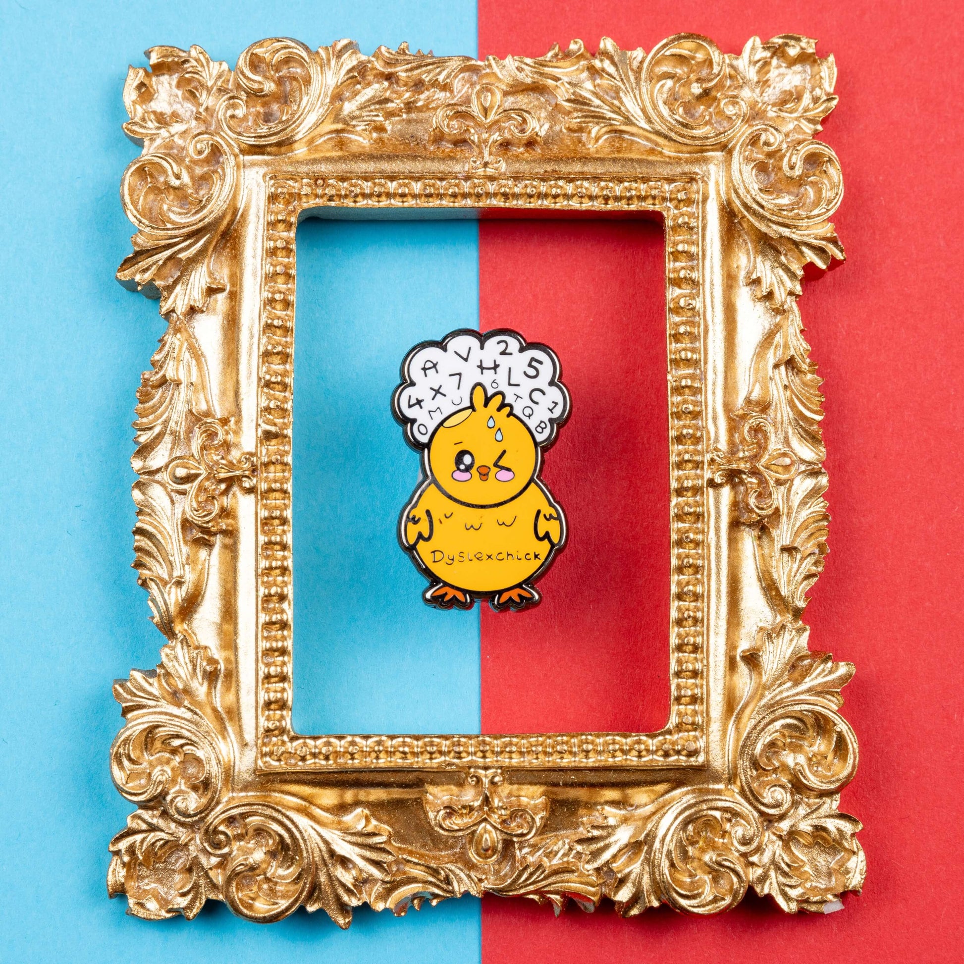 The Dyslexchick Enamel Pin - Dyslexia on a red and blue background inside a gold ornate frame. A yellow confused chick shaped pin badge with a thought bubble above its head full of letters and numbers with 'dyslexchick' written across its middle. The hand drawn design is raising awareness for dyslexia.