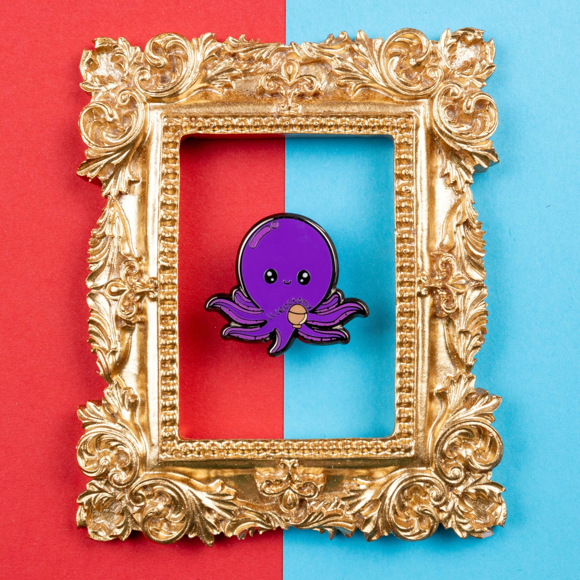 Ileoctomy Enamel Pin - Ileostomy on a blue and red card background inside a gold ornate frame. The enamel pin is a cute smiling purple octopus sticker with text saying ileoctomy on its belly with a stoma bag underneath. Enamel pin designed to raise awareness for Ileostomy.