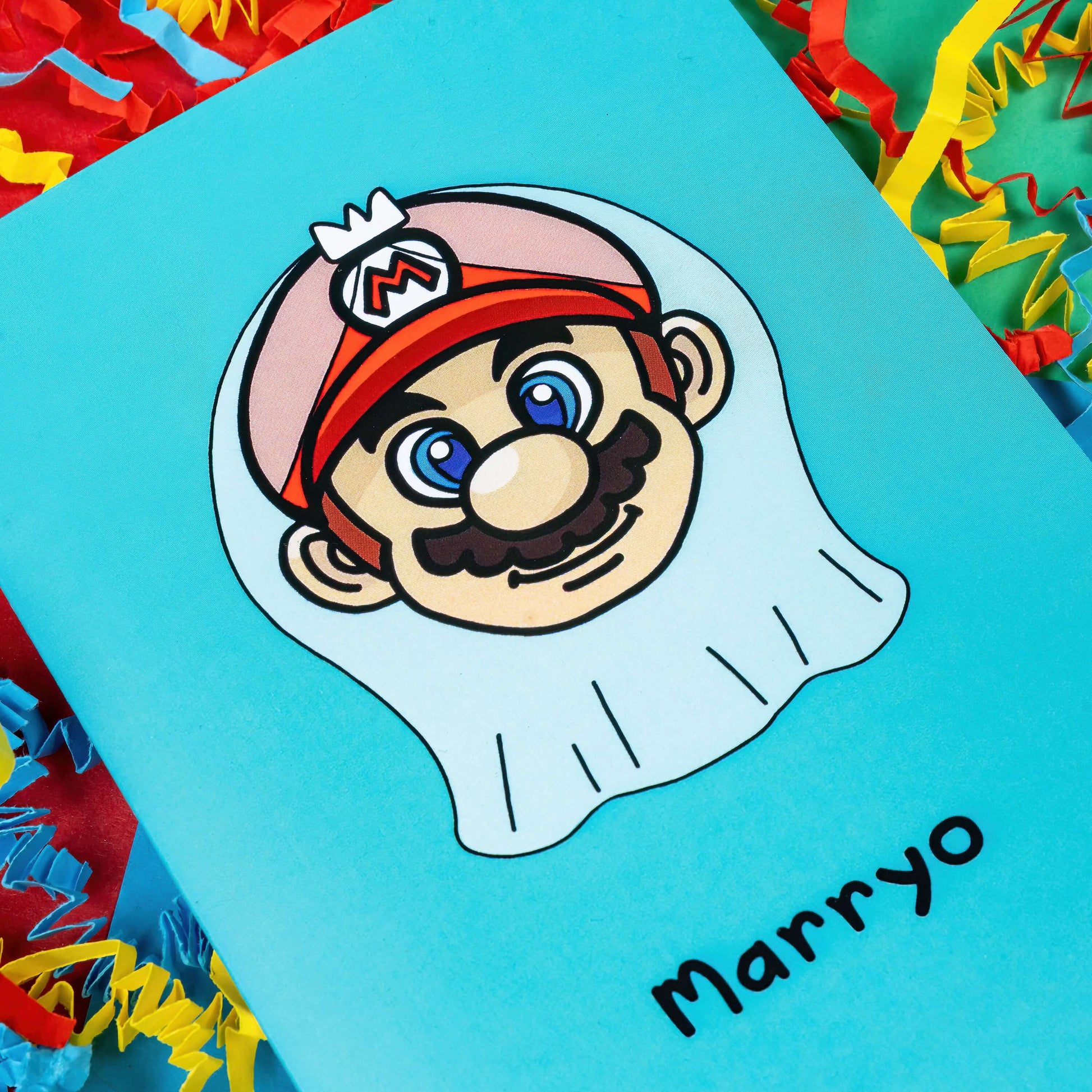 The Marryo - Mario Engagement Wedding Card on a red, blue and green background with red, yellow and blue crinkle card confetti. The blue a6 congratulations card features a smiling nintendo mario character head wearing a white bridal wedding veil, underneath him is black text reading 'Marryo'.
