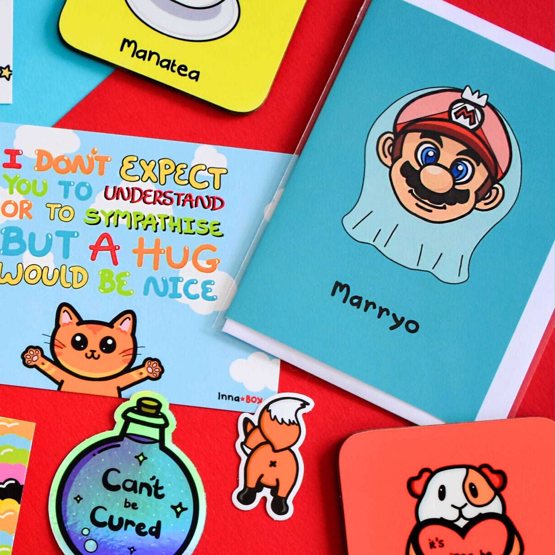 The Marryo - Mario Engagement Wedding Card on a red background with other innabox products. The blue a6 congratulations card features a smiling nintendo mario character head wearing a white bridal wedding veil, underneath him is black text reading 'Marryo'.