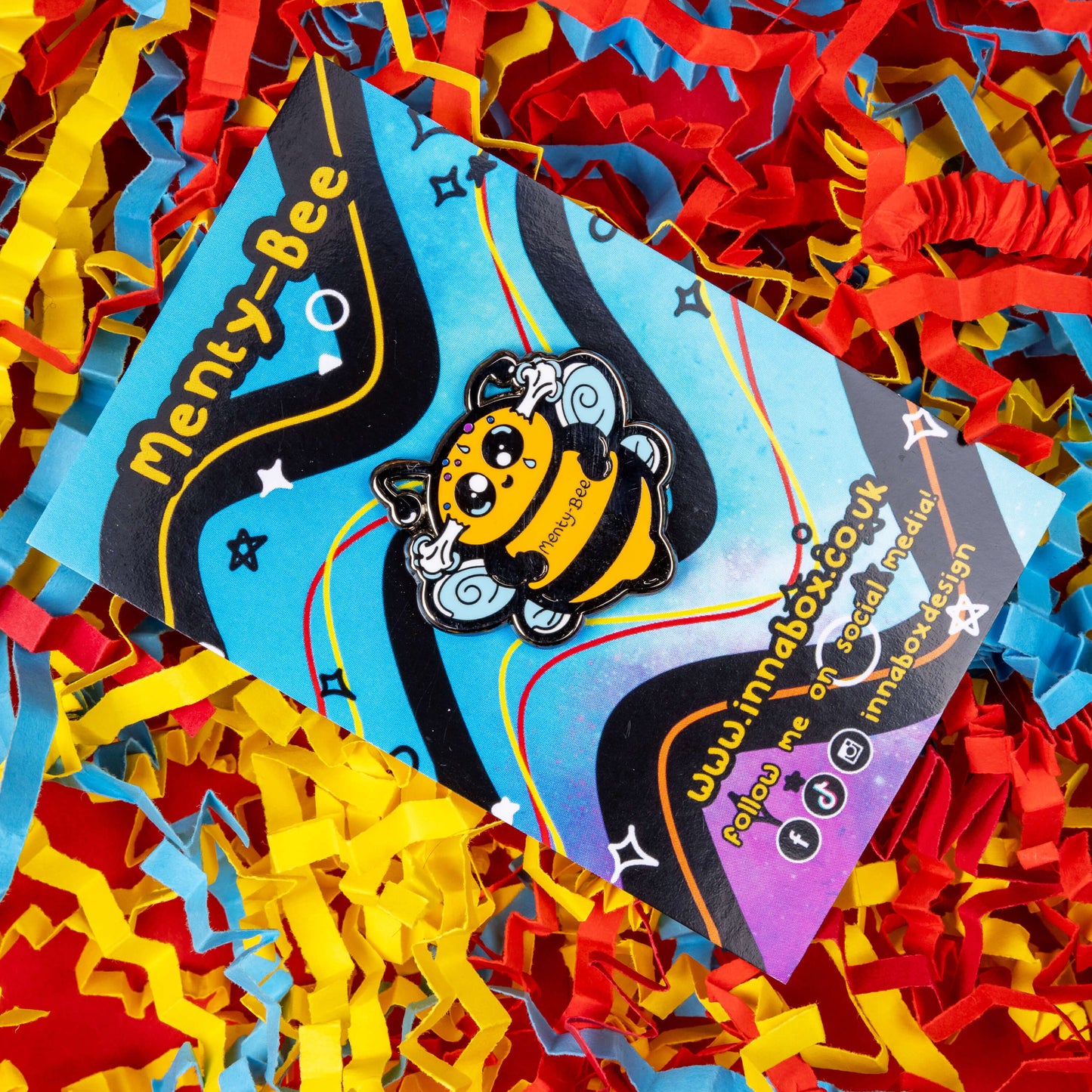 Menty-Bee Enamel Pin - Mental Breakdown pinned to its backing card with card confetti in the background. The enamel pin is of a bee looking stressed with steam coming out of its head and the text menty-Bee on its chest. Hand drawn design made to raise awareness for mental breakdowns