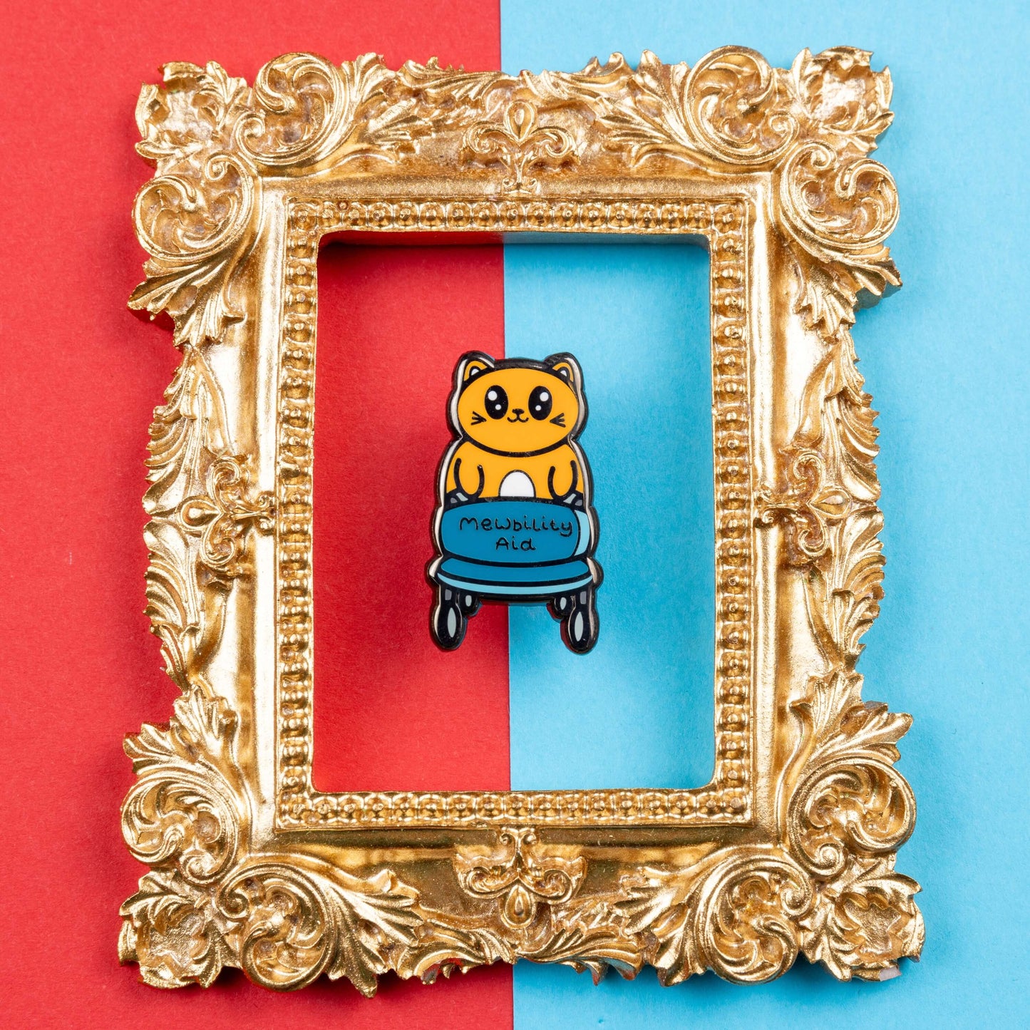 The Mewbility Aid Cat Enamel Pin - Mobility Aid on red and blue card in a gold ornate frame. An orange smiling cat walking upright with a blue mobility aid, across the walking chair reads 'mewbility aid'. The hand drawn designs is raising awareness for mobility aids.