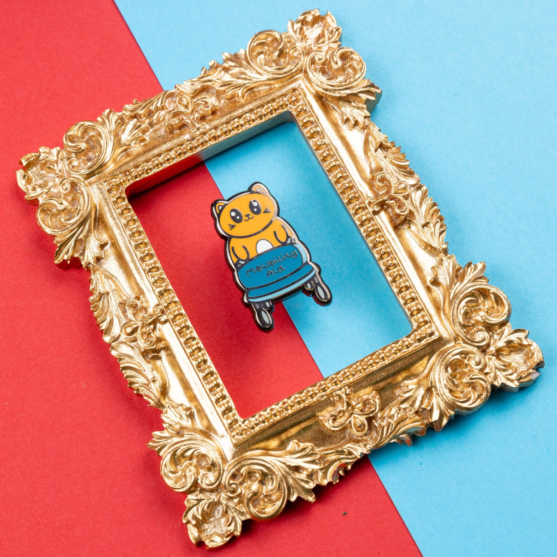 The Mewbility Aid Cat Enamel Pin - Mobility Aid on red and blue card in a gold ornate frame. An orange smiling cat walking upright with a blue mobility aid, across the walking chair reads 'mewbility aid'. The hand drawn designs is raising awareness for mobility aids.