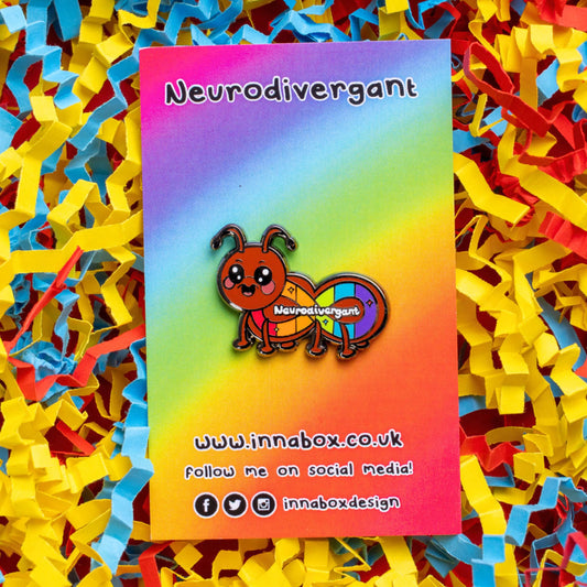 The Neurodivergant Ant Enamel Pin - Neurodivergent on rainbow backing card with innabox social media handles along the bottom laid on a blue, yellow and red card confetti background. The brown ant shape enamel pin is smiling with a rainbow infinity symbol and white text reading 'neurodivergant' with sparkles across its body. The hand drawn design is raising awareness for neurodiversity.