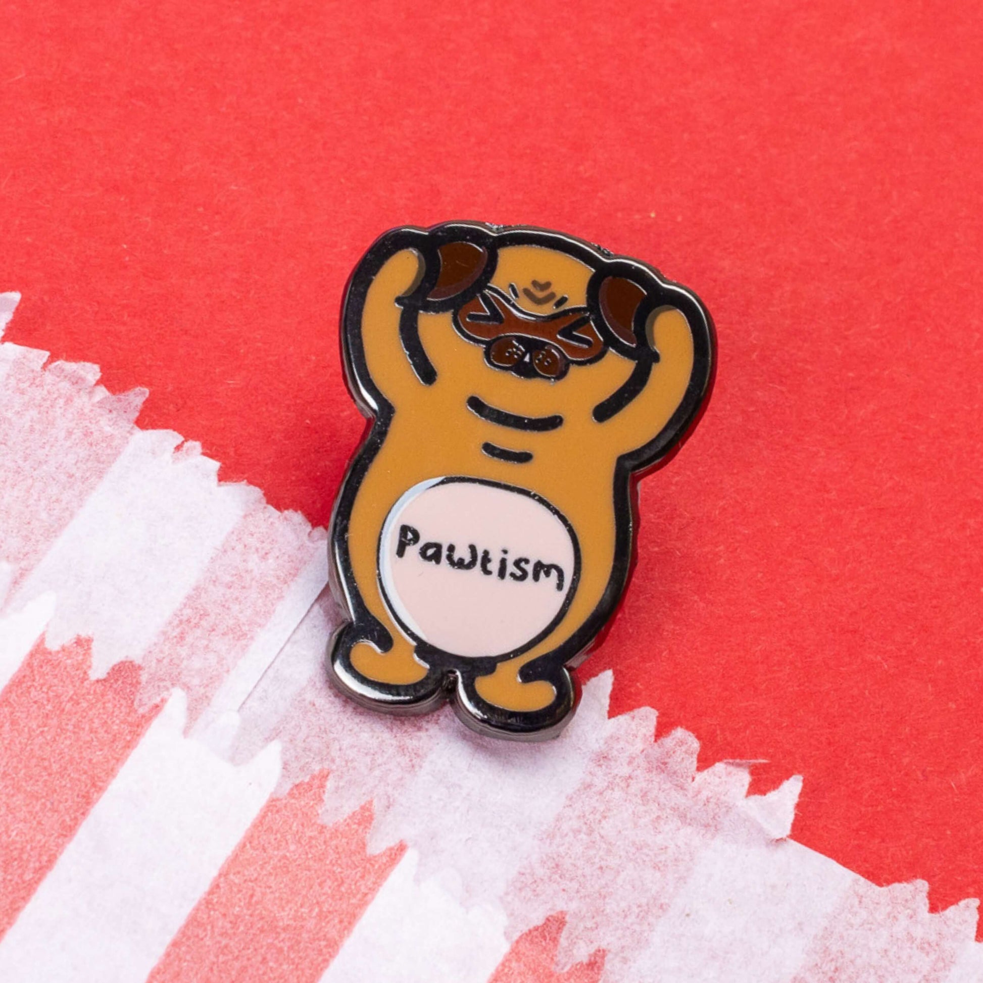 Pawtism Enamel Pin - Autism on a red card background. The enamel pin is of a brown pug with its hands on its ears and the word pawtism written across its belly. The enamel pin is to raise awareness for neurodiversity and autism.