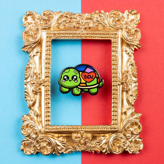 The Speshell Educational Needs Enamel Pin - SEN - Special Educational Needs on a red and blue background in a gold ornate frame. A rainbow shell kawaii cute style tortoise with pink cheeks and sparkling eyes, on its shell is a red heart with 'SEN' in the middle. The pin design is raising awareness for SEN Special Educational Needs.