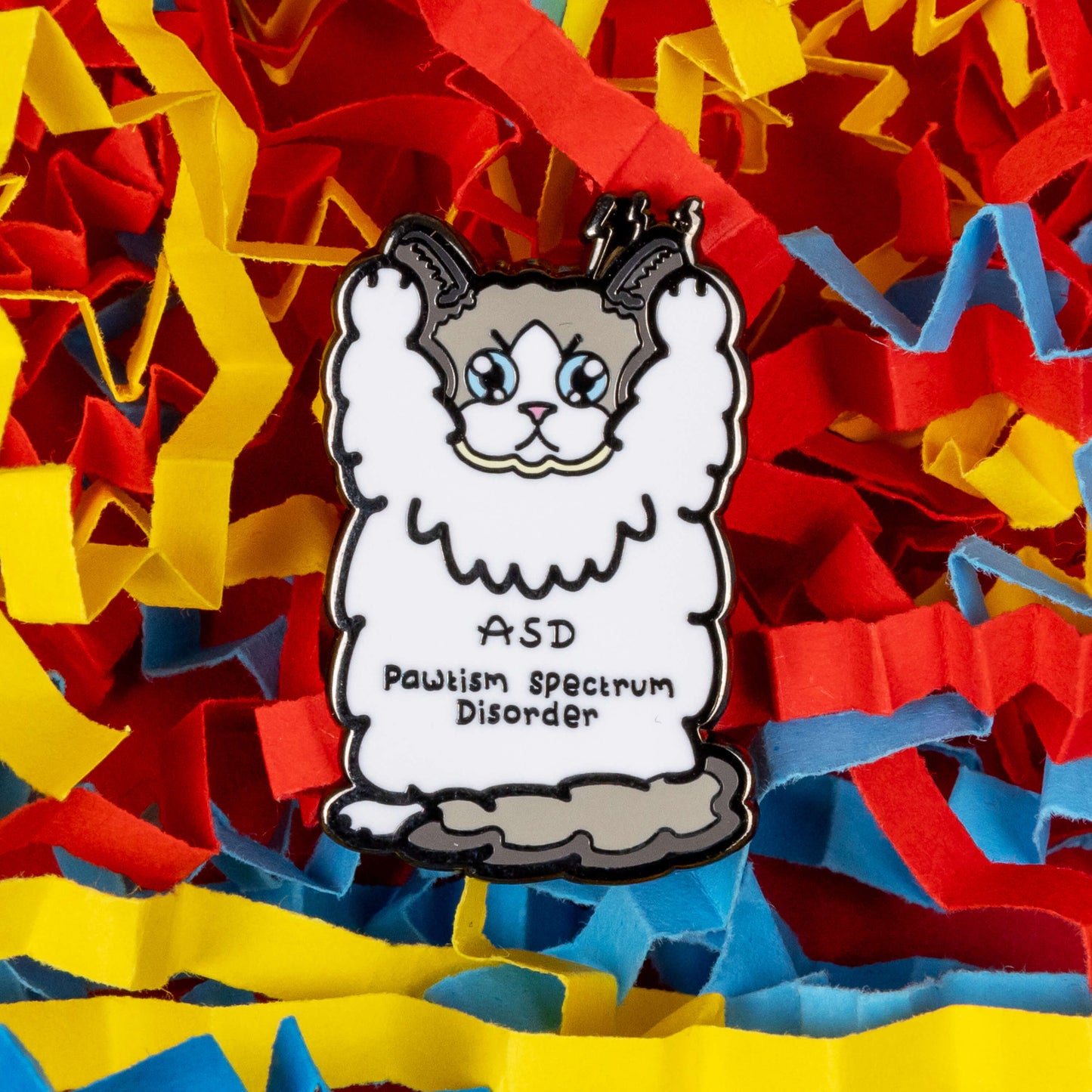 Pawtism Spectrum Disorder Cat Enamel Pin - Autism Spectrum Disorder (ASD) on a blue, yellow and red coloured card confetti background. The pin is of a grey and white cat with a stern expression and paws in the air. 'ASD Pawtism Spectrum Disorder' is written across it's stomach in black text. Hand drawn design to raise awareness for Autism Spectrum Disorder (ASD)