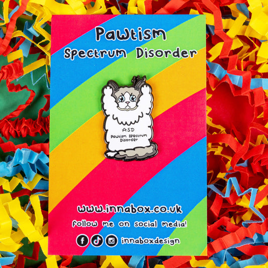 Pawtism Spectrum Disorder Cat Enamel Pin - Autism Spectrum Disorder (ASD) on it's rainbow striped backing card with Innabox social media handles written on it. It is resting on a blue, yellow and red coloured card confetti background. The pin is of a grey and white cat with a stern expression and paws in the air. 'ASD Pawtism Spectrum Disorder' is written across it's stomach in black text. Hand drawn design to raise awareness for Autism Spectrum Disorder (ASD)