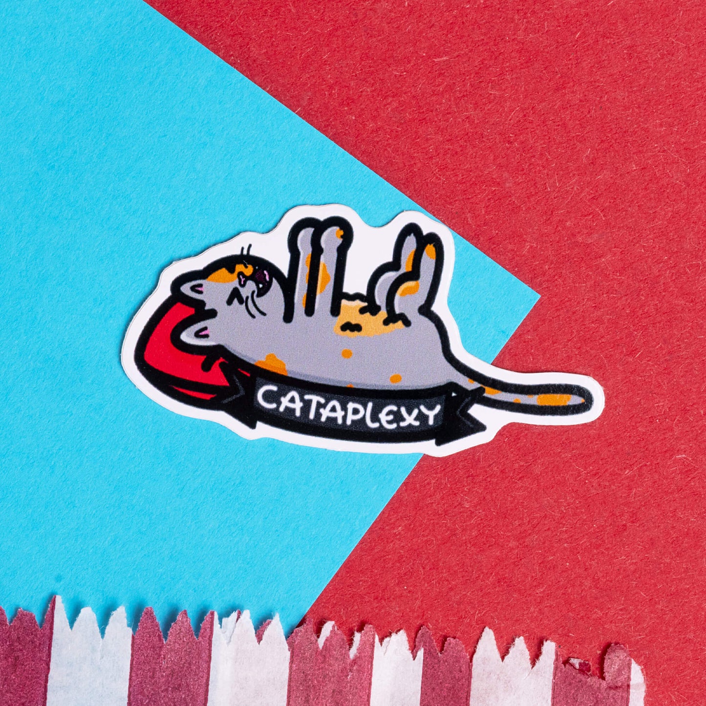 Innabox sticker displaying a cartoon cat lying upside down with 'Cataplexy' written below. The sticker is set against a bright background with contrasting red and blue paper. Innabox designs products that celebrate and uplift individuals with chronic illnesses or hidden disabilities.