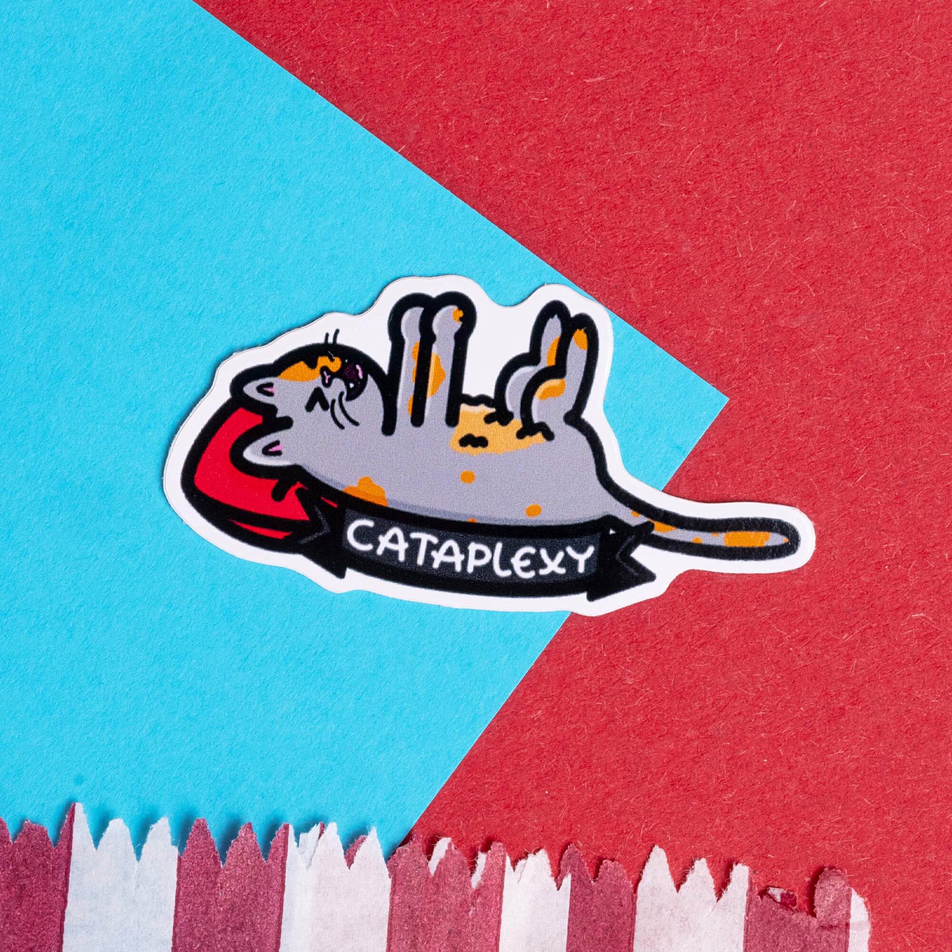 Innabox sticker displaying a cartoon cat lying upside down with 'Cataplexy' written below. The sticker is set against a bright background with contrasting red and blue paper. Innabox designs products that celebrate and uplift individuals with chronic illnesses or hidden disabilities.