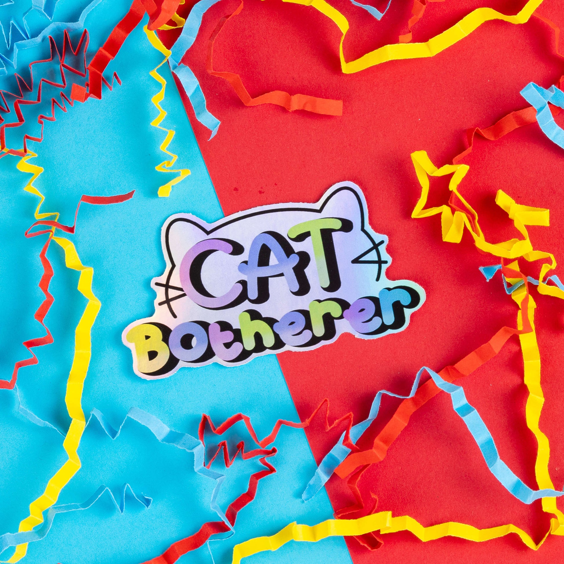 Innabox sticker with the phrase 'Cat Botherer' in playful, colourful lettering, outlined with subtle cat ears and whiskers. Set against a backdrop of vibrant red, blue, and yellow paper confetti