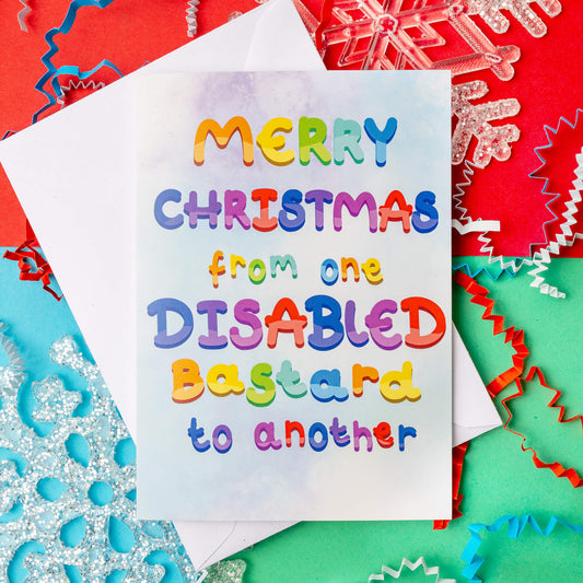 Merry Christmas from one disabled bastard to another card by Innabox. The card features bright rainbow lettering on a pastel background. Perfect for disabled individuals looking for humour and connection during the holiday season. Decorative snowflakes and colourful confetti surround the card, set against a festive red and green backdrop.