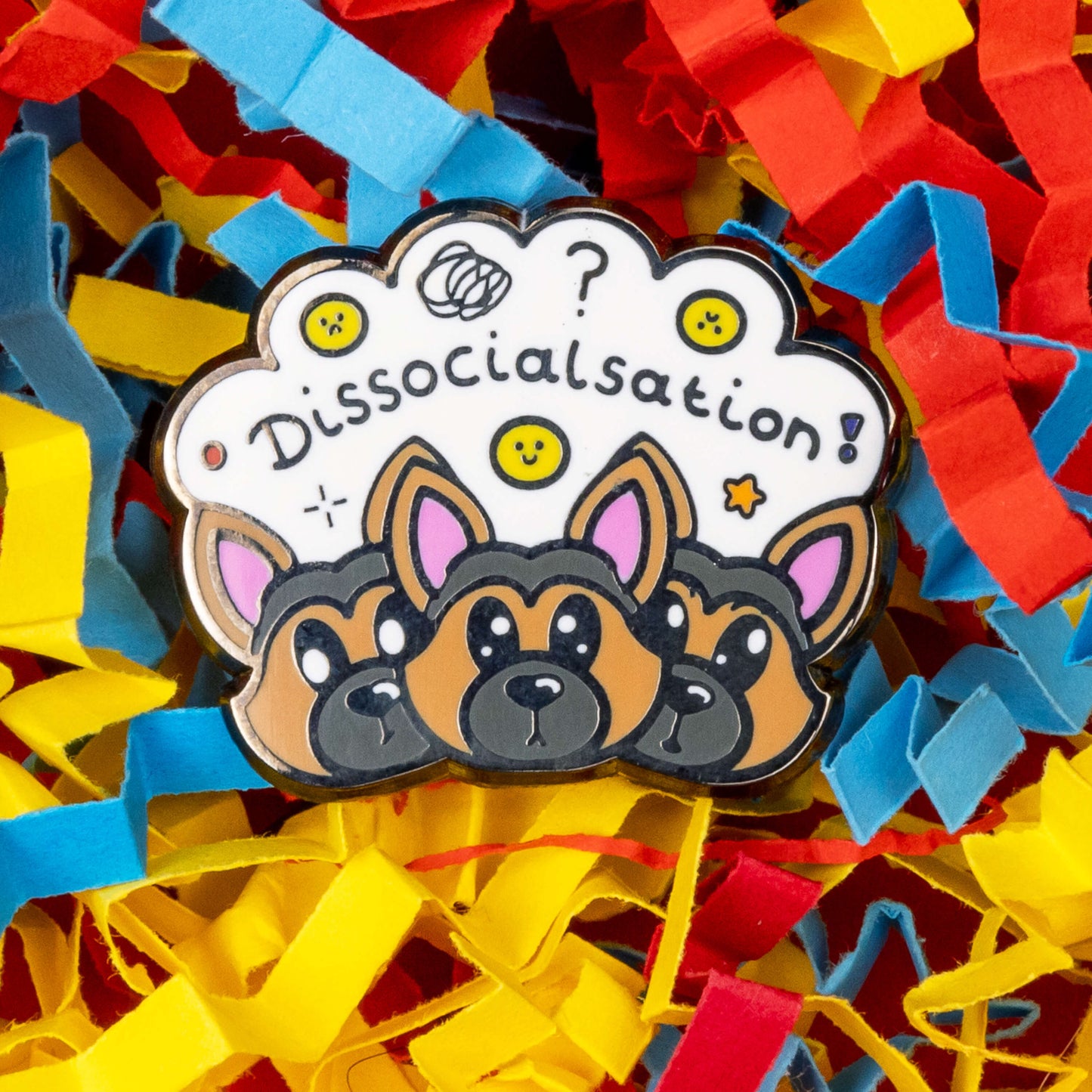 The Dissocialsation Enamel Pin - Dissociation on a red, blue and yellow card confetti background. Three confused brown and black Alsatian dog heads with their ears perked up, above them is a white cloud with sad and happy yellow faces, sparkles, question marks and black text reading 'dissocialsation!'. The design is raising awareness for dissociation.