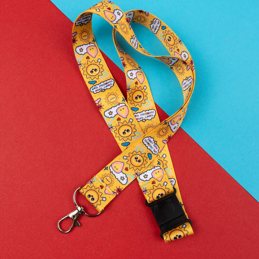 Yellow lanyard with cheerful sun and cloud designs, and motivational phrases to avoid burnout. Designed to promote awareness for invisible illnesses and hidden disabilities. Includes a black safety buckle and metal clasp. Displayed on a red and blue geometric background.