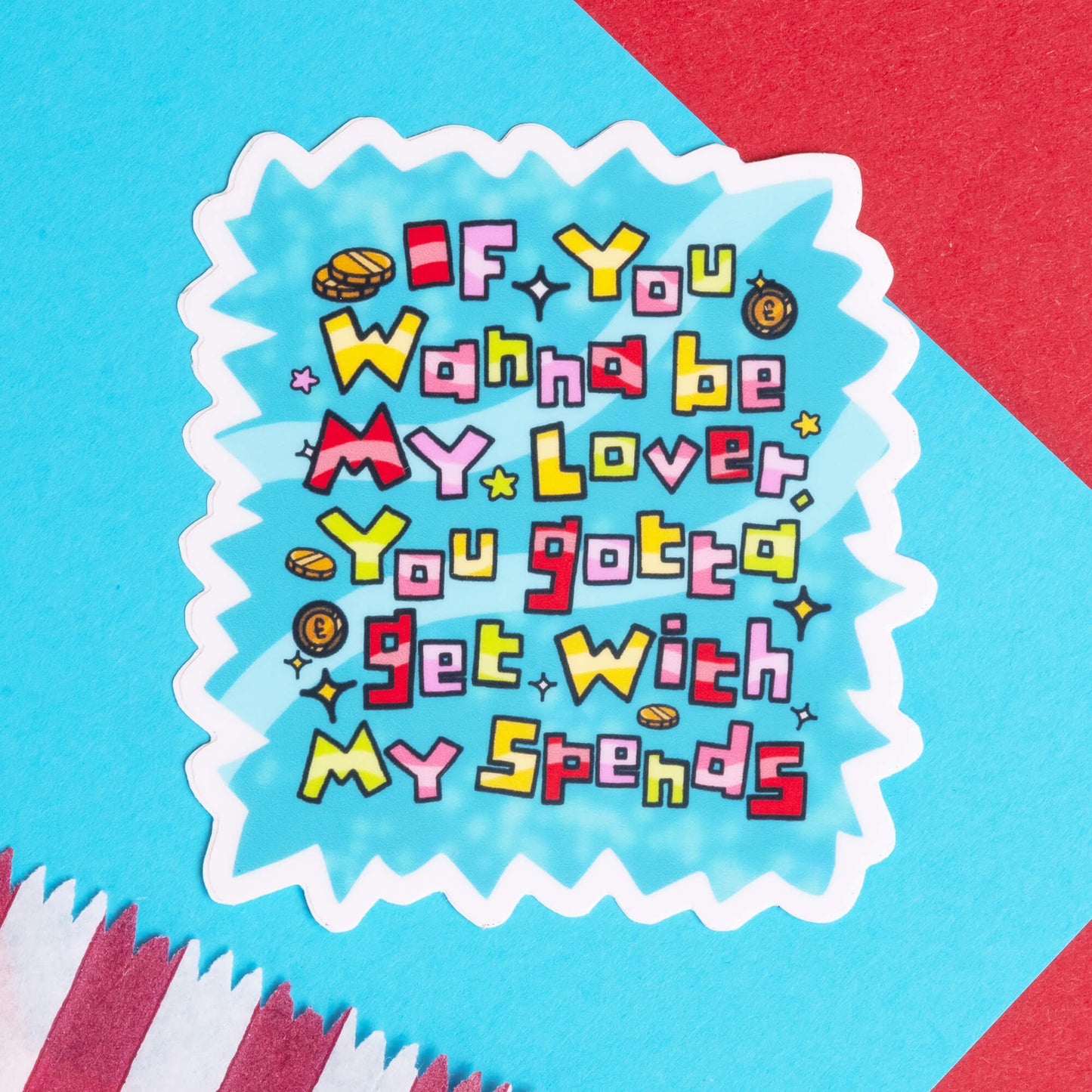 A vibrant sticker by Innabox displaying the message, "If you wanna be my lover, you gotta get with my spends," in a fun, pixelated font. The sticker has a jagged white border, a light blue background, and small icons of coins surrounding the text. The sticker is photographed on a colourful background with blue, red, and white elements. This product is designed to support and uplift those with chronic illnesses or hidden disabilities.