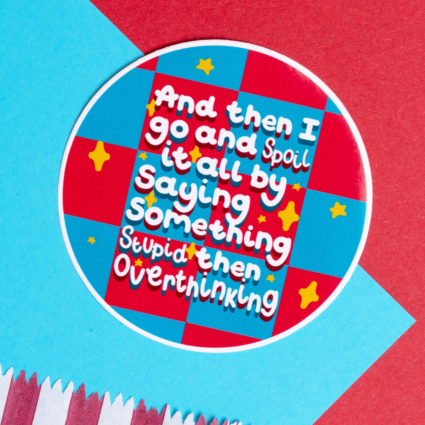 Bright and bold Innabox sticker with the phrase 'And then I go and spoil it all by saying something stupid then overthinking.' The design features a red and blue checkered background with yellow stars, placed on a contrasting red and blue paper surface, ideal for people with hidden disabilities or chronic illnesses who resonate with the anxiety of overthinking.