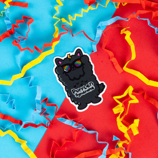 Innabox sticker featuring a fluffy black cat with rainbow sunglasses and a lightning bolt on its head, with the text 'Purrlen Syndrome.' The cat has a quirky, confident expression, with raised paws as if celebrating its uniqueness. Surrounded by colourful red, blue, and yellow paper confetti. Designed to spread awareness and celebrate the strength of those living with Irlen Syndrome.