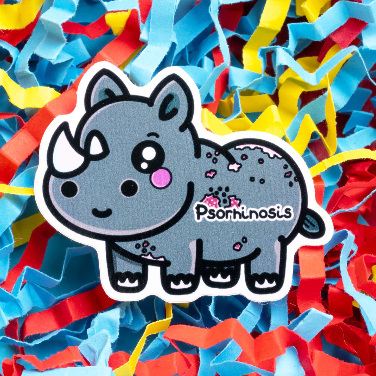 Innabox Psoriasis Rhino hand drawn sticker depicting an adorable grey rhino with white horns and pink spots symbolising psoriasis. The word 'Psorhinosis' is featured on the rhino's side. The colourful, shredded paper background adds a playful contrast, enhancing this disability-inspired product aimed at empowering individuals with chronic illnesses