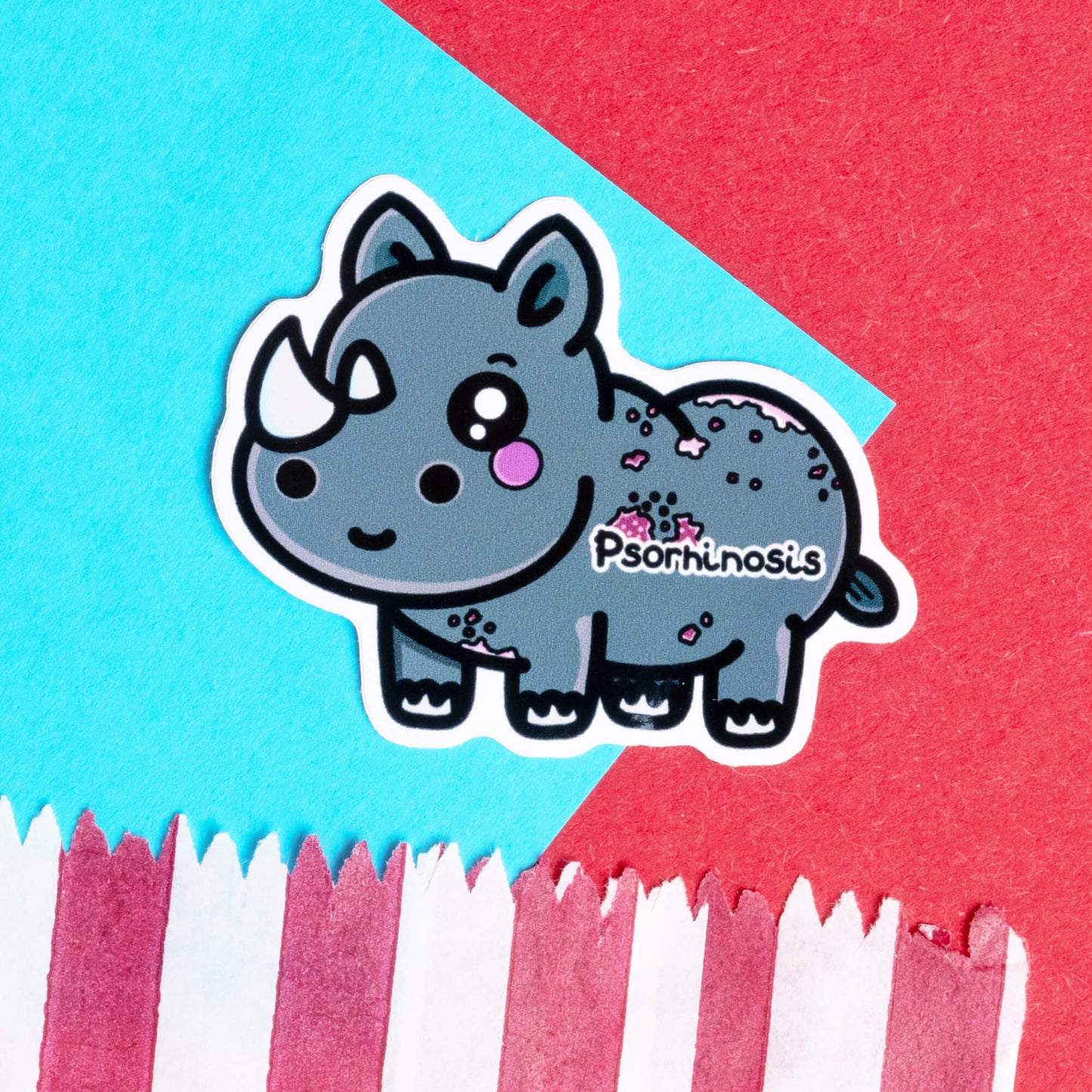 Innabox Psoriasis Rhino hand drawn sticker featuring a cute, grey rhino character with white horns and pink spots, representing psoriasis. The sticker has the word 'Psorhinosis' on it and is set against a vibrant red and blue geometric background. Designed to uplift those with chronic illnesses, this disability-inspired product promotes awareness and positivity