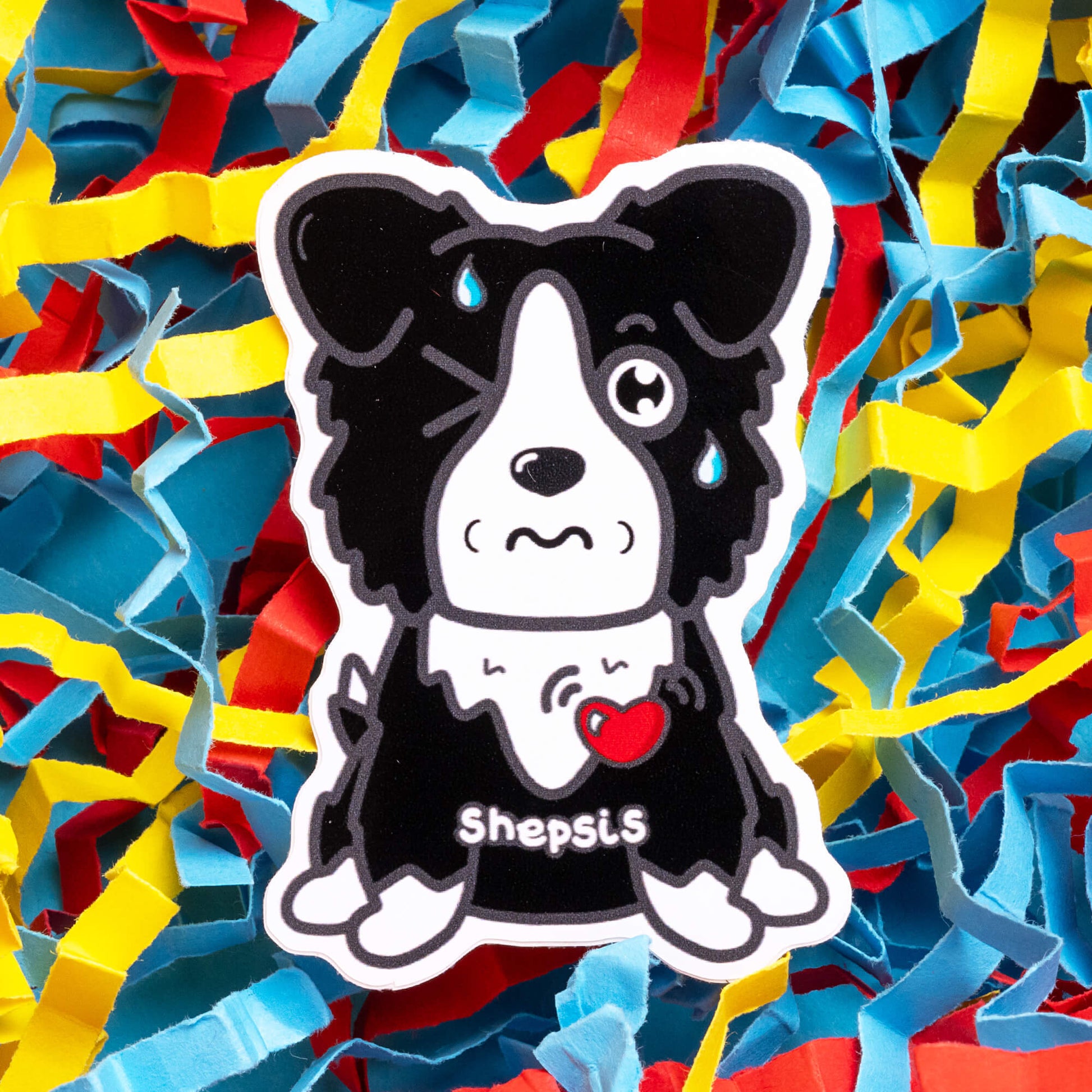 Innabox sticker showing a cartoon sheepdog with a black and white fur pattern, a wincing shut eye, and a teardrop. The word 'Shepsis' is printed on its chest, a pun to highlight sepsis awareness. The dog has a red heart symbol, representing love and support for those with chronic conditions or hidden disabilities. The background is filled with vibrant, shredded paper in red, yellow, and blue, enhancing the sticker's eye-catching design and message.