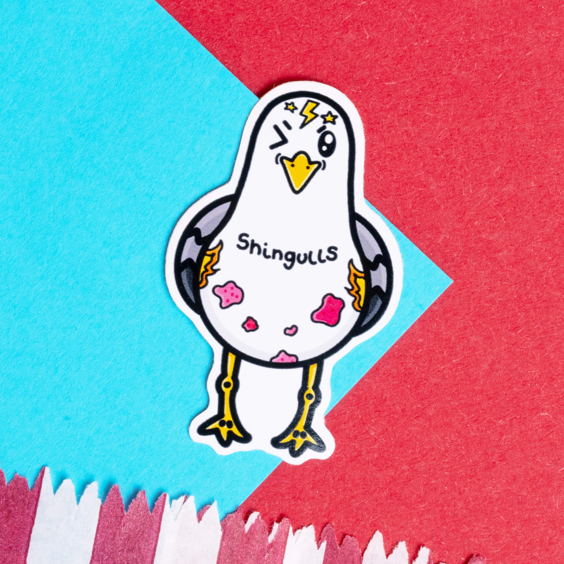 Innabox Shingulls sticker featuring a hand drawn seagull character with lightning bolts and pink patches, representing shingles. The sticker has 'Shingulls' text and is set against a bold red and blue geometric background. This disability-inspired product is designed to raise awareness and provide support for those with chronic illnesses.