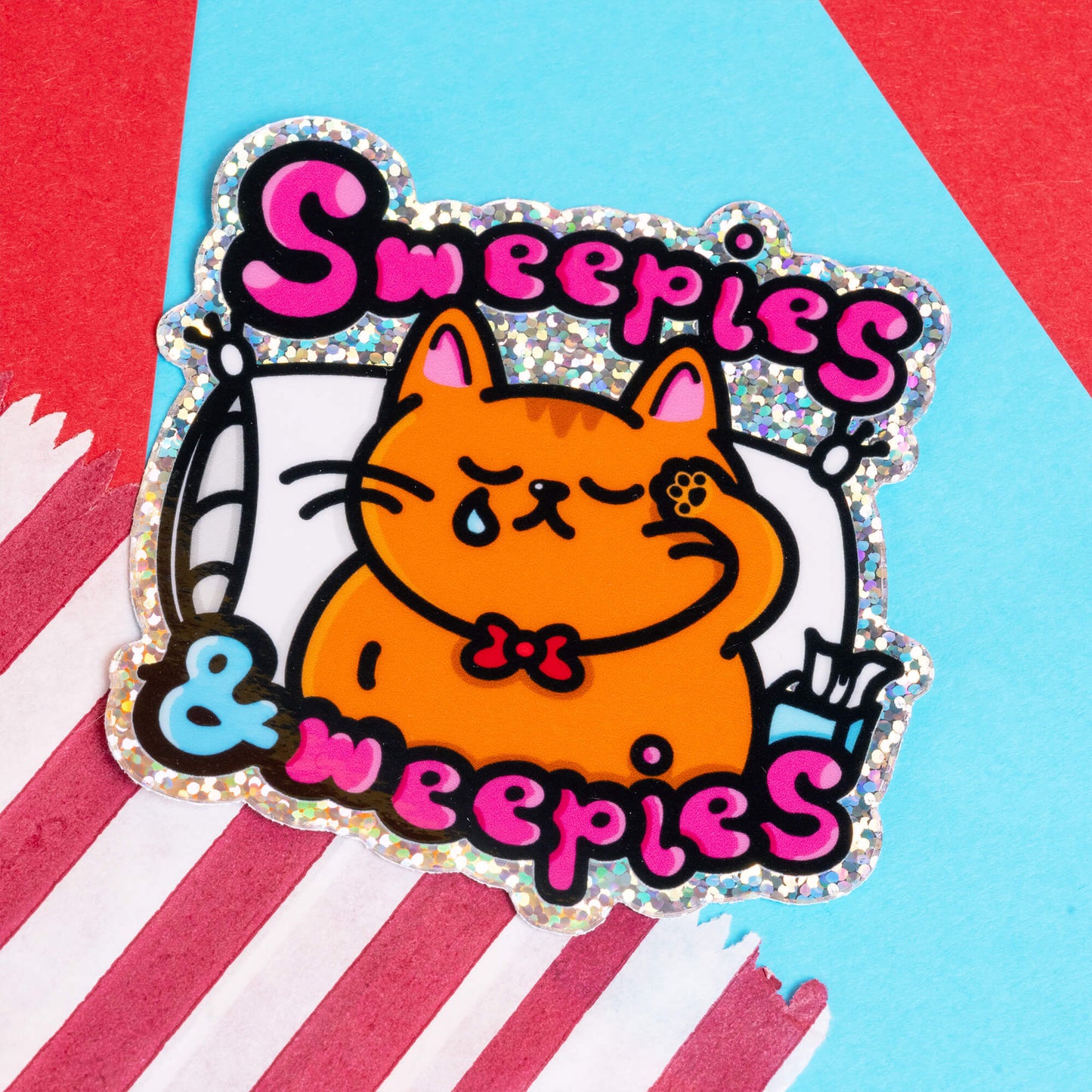 A vibrant sticker by Innabox featuring an orange cat with a tear, labelled "Sweepies & Weepies" in bold, pink and black letters. The cat is resting with a pillow and a tissue box in a colourful background filled with blue, yellow, and red shredded paper. This sticker represents the challenges faced by individuals with chronic illnesses or hidden disabilities, designed to uplift and resonate with those experiencing similar struggles.