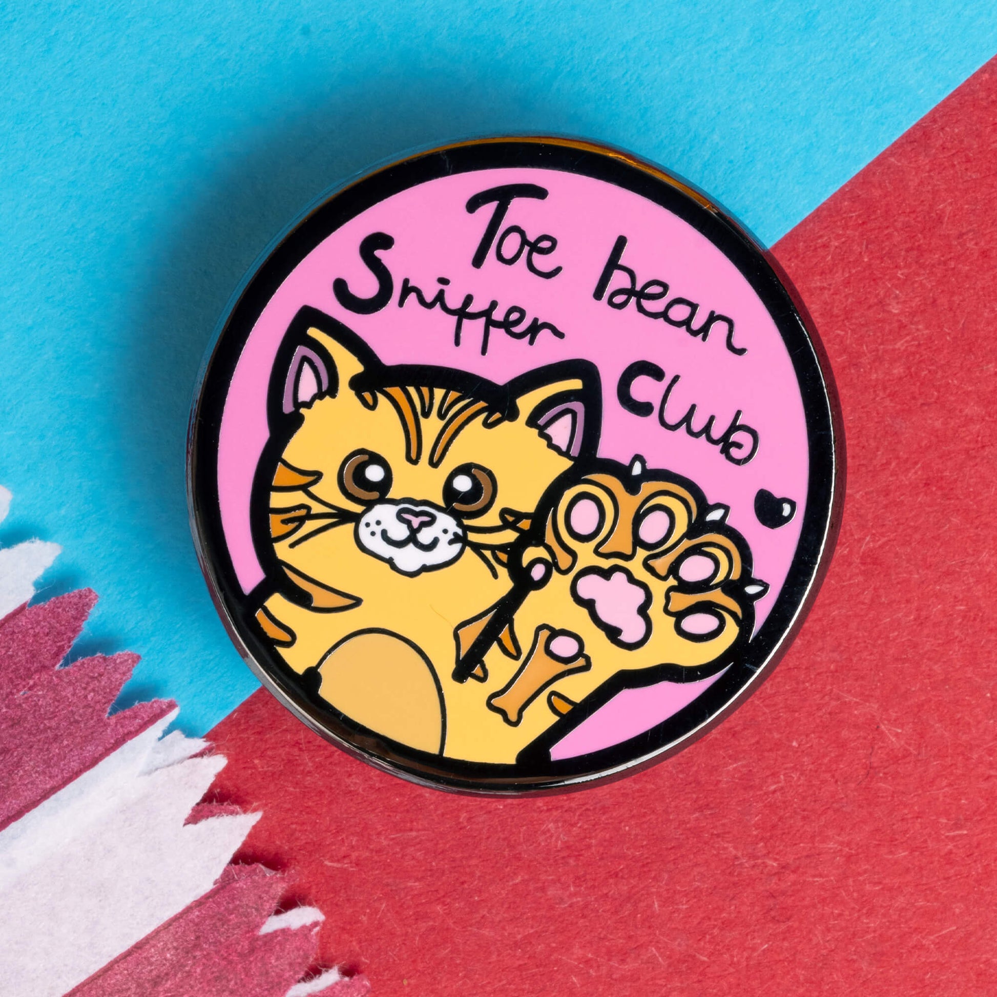 Innabox pin badge featuring a cute orange cat raising a paw with visible pink toe beans. The badge reads 'Toe Bean Sniffer Club' in playful text on a pink background, perfect for cat lovers. This product from Innabox celebrates disability awareness and aims to uplift those with chronic illnesses or hidden disabilities.